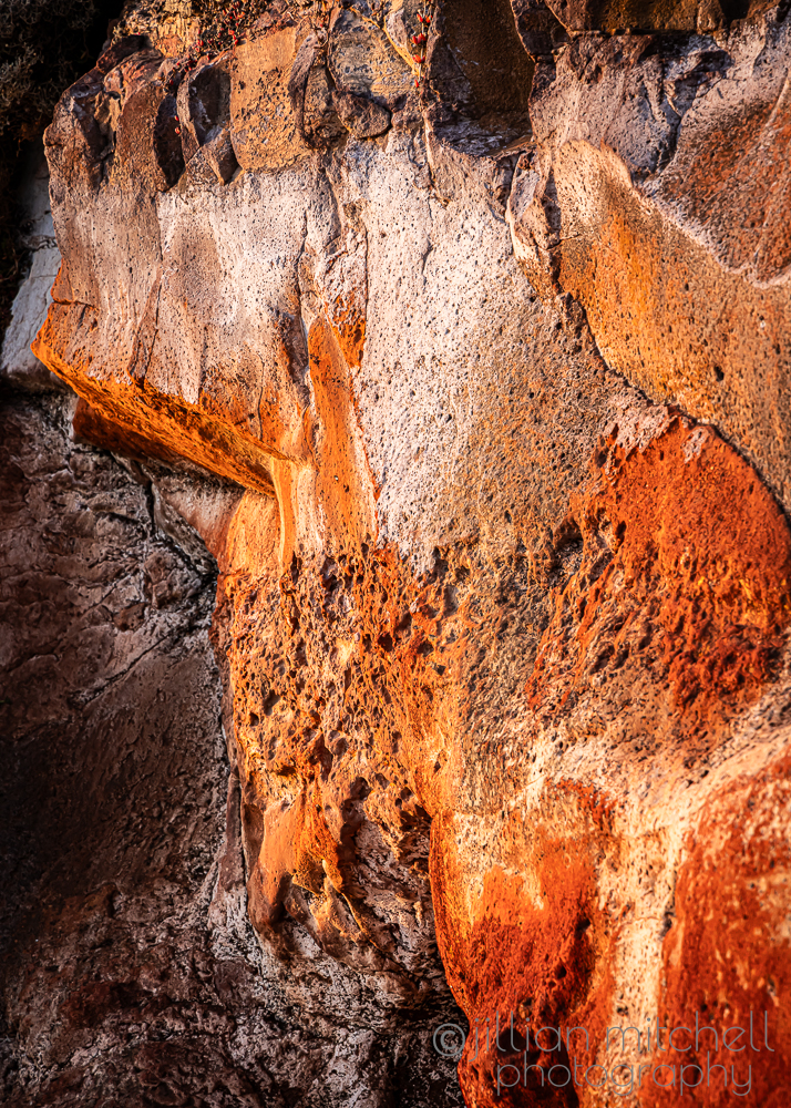 Close up photo of natural honeycomb tafoni weathering in a volcanic cliff face at Surf Beach on Phillip Island showing deep ochre orange pockets, shadows and textured salt erosion cavities.