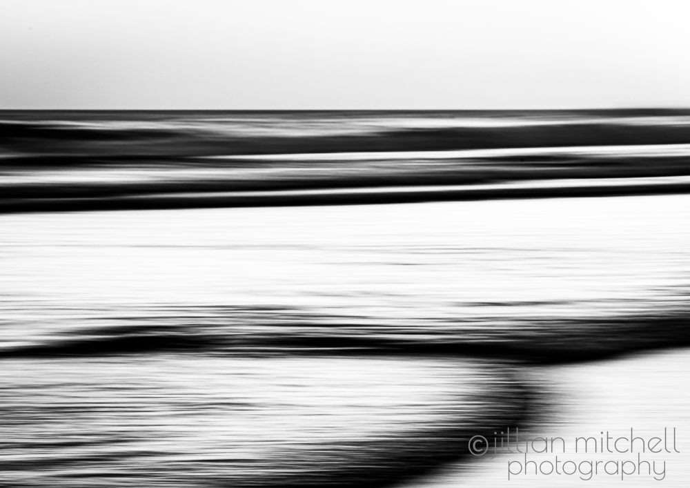 Minimalist monochrome ocean image using slow shutter and intentional camera movement to create smooth, abstract wave motion.